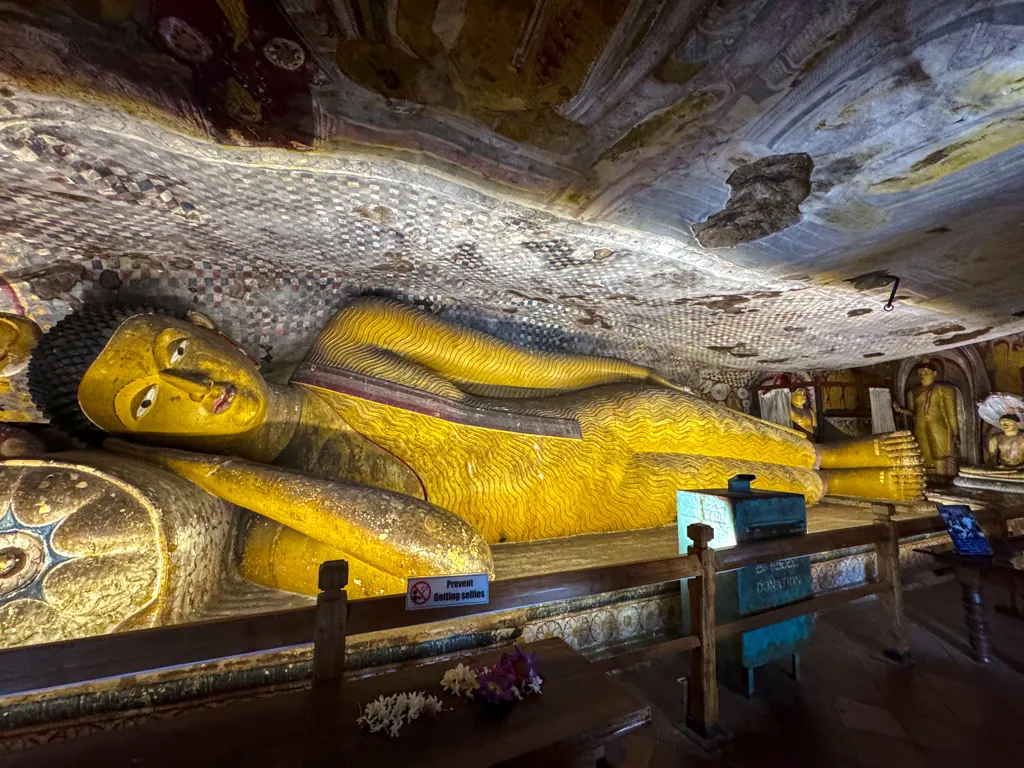A row of seated stone Buddha figures along the wall of a Dambulla cave, lit from the entrance